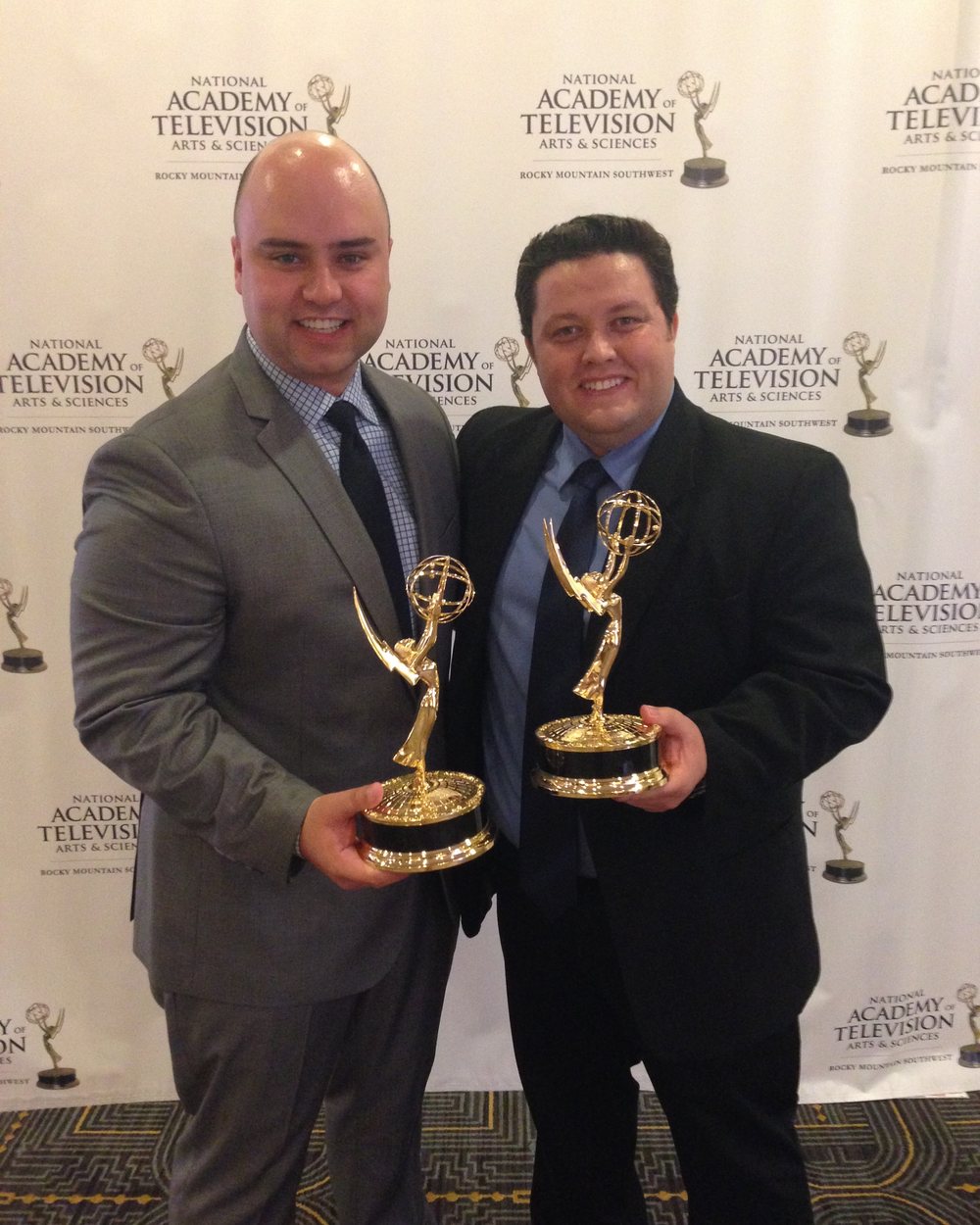 Daniel Souza and Luiz Malaman each holding an Emmy statuette in front of the National Academy of Television Arts and Sciences backdrop